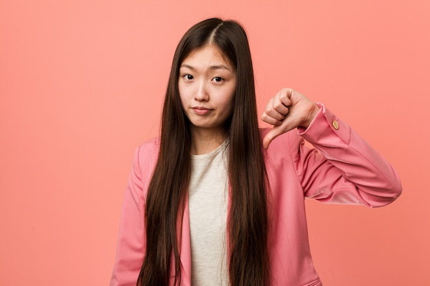 Junge chinesische Geschäftsfrau, die den rosa Anzug zeigt eine Abneigungsgeste, Daumen unten trägt. Uneinigkeit Konzept.