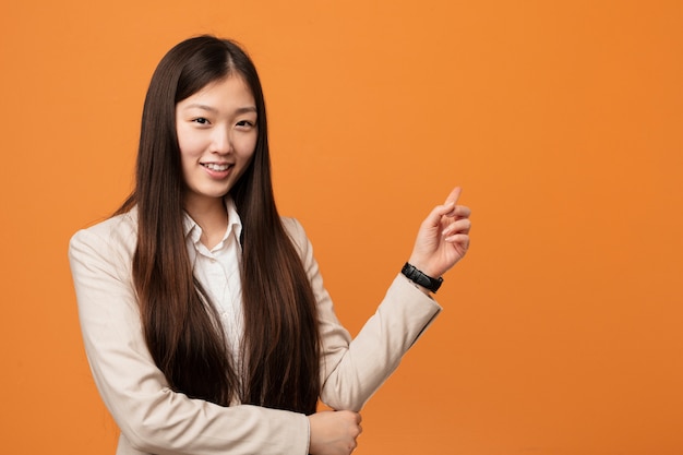 Junge chinesische Geschäftsfrau, die mit dem Zeigefinger weg nett zeigen lächelt.