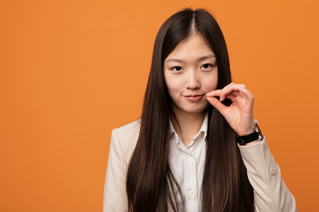 Junge chinesische Geschäftsfrau mit den Fingern auf den Lippen, die ein Geheimnis halten.