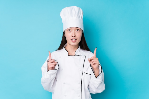 Junge chinesische Kochfrau lokalisiert, die oben mit geöffnetem Mund zeigt.