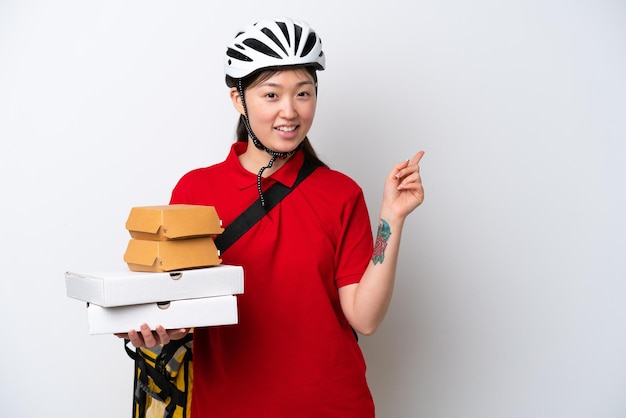 Junge chinesische Lieferfrau, die Essen zum Mitnehmen isoliert auf weißem Hintergrund nimmt und mit dem Finger zur Seite zeigt