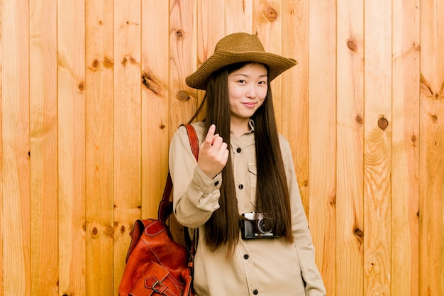 Junge chinesische Reisendfrau, die mit dem Finger auf Sie zeigt, als ob Einladung näher kommen.