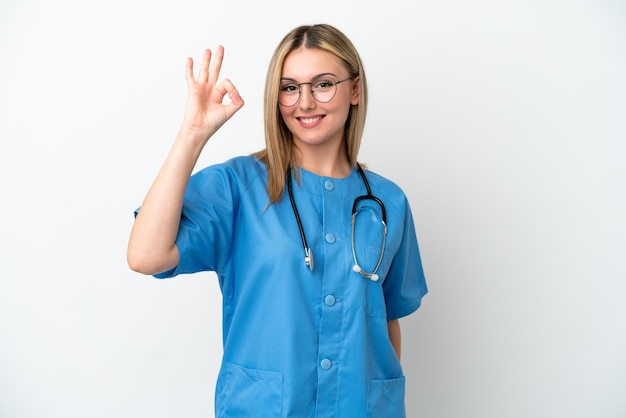Junge Chirurgin, Ärztin, isoliert auf weißem Hintergrund, die mit den Fingern ein Ok-Zeichen zeigt