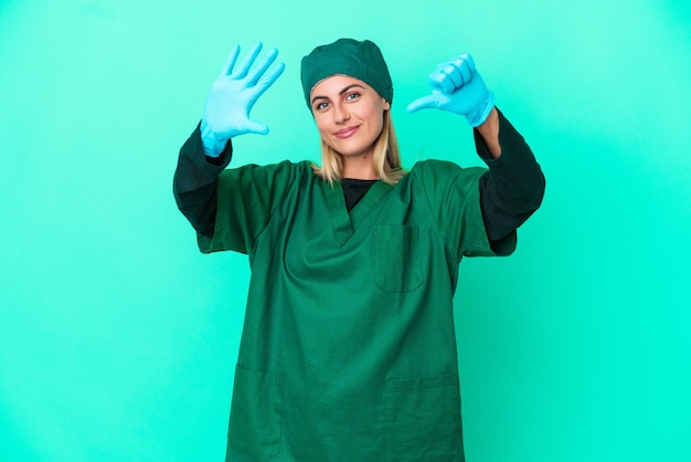 Junge Chirurgin aus Uruguay in grüner Uniform isoliert auf blauem Hintergrund, die sechs mit den Fingern zählt