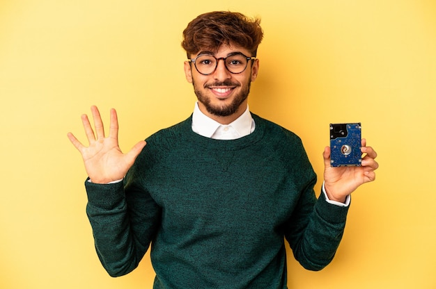 Junge Computer-Mann isoliert auf gelbem Hintergrund lächelnd fröhlich zeigt Nummer fünf mit den Fingern.