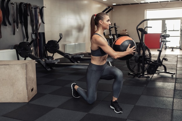 Junge Crossfit-Frau, die in der modernen Turnhalle mit Medizinball trainiert. Funktionstraining. Gesunder Lebensstil