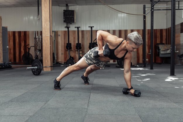 Junge Crossfit-Frau trainiert mit Dummköpfen. Liegestütze. Funktionstraining