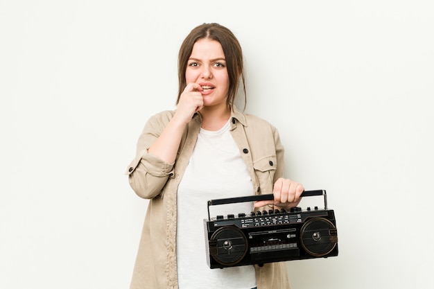 Junge curvy Frau, die beißende Fingernägel eines Retro- Radios, nervös und sehr besorgt hält.