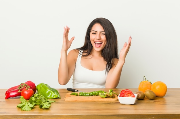 Junge curvy Frau, die eine gesunde Mahlzeit empfängt eine angenehme Überraschung, aufgeregt und Hände anhebend vorbereitet.