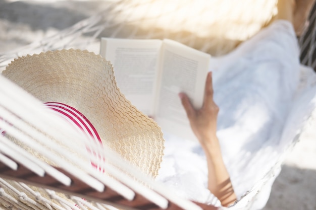 Junge Dame, die ein Buch in der Hängematte auf tropischem sandigem Strand liest.