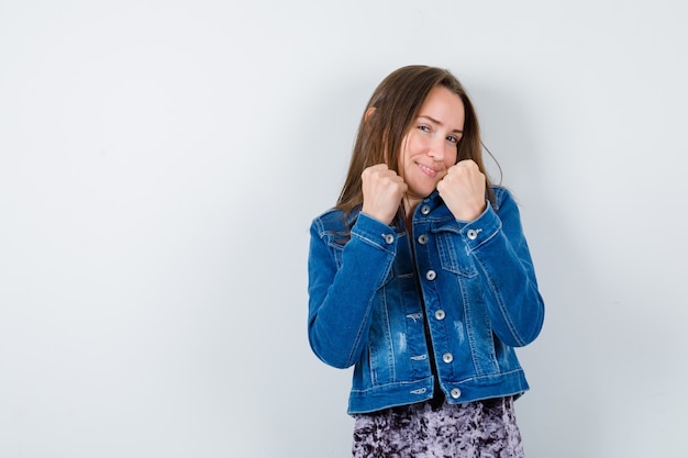 Junge Dame, die in der Kampfpose in Bluse, Jeansjacke steht und selbstbewusst aussieht. Vorderansicht.