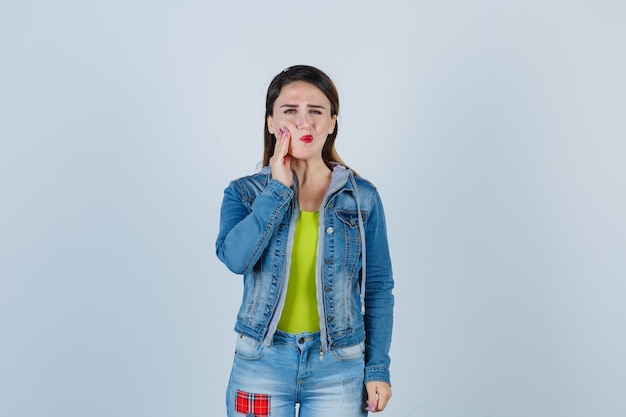 Junge dame, die unter schrecklichen zahnschmerzen in denim-outfit leidet und belästigt aussieht. vorderansicht.