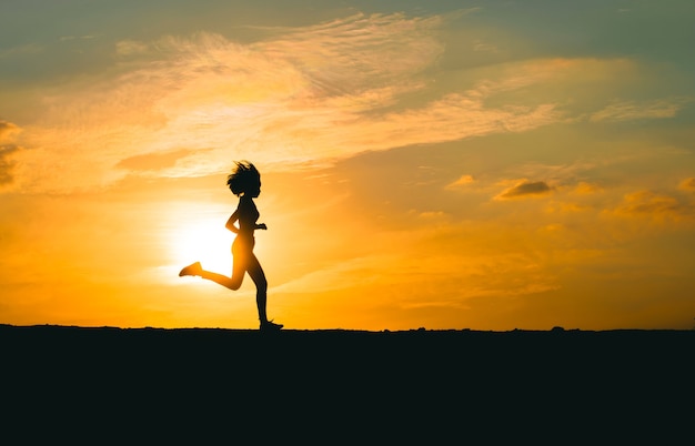 Junge Dame, die während des Sonnenuntergangs auf einer Landstraße läuft