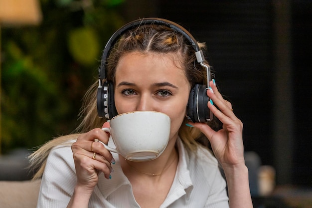 Junge Dame hört Musik mit ihren Kopfhörern und trinkt Tee