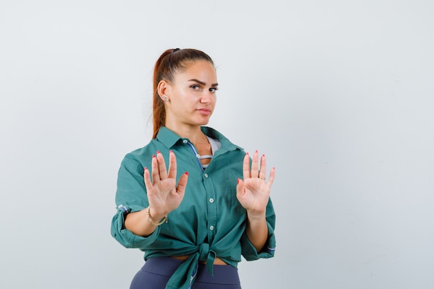 Junge Dame im Hemd, Hose, die Stoppgeste zeigt und unzufrieden aussieht, Vorderansicht.