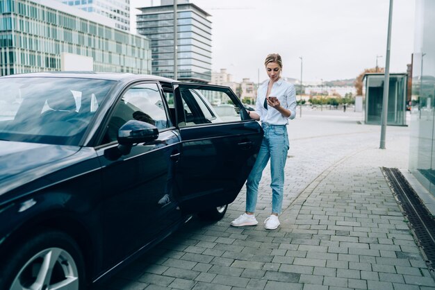 Junge Dame mit Handy vor dem Einsteigen ins Auto