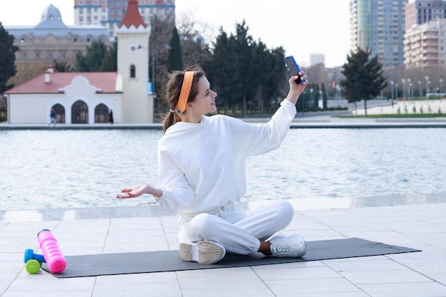 Junge Dame sitzt auf der Yogamatte und macht Selfie Hochwertiges Foto