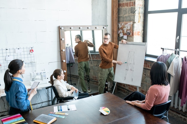 Junge deaktivieren männliche Designer, die auf die Skizze auf dem Whiteboard zeigen, während sie Kollegen ihre Sicht der neuen Kollektion präsentieren