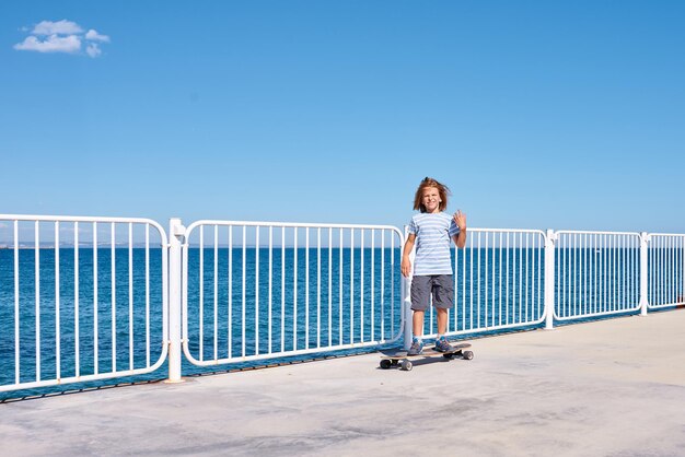 Junge, der an einem sonnigen Tag ein Longboard auf einem Pier reitet