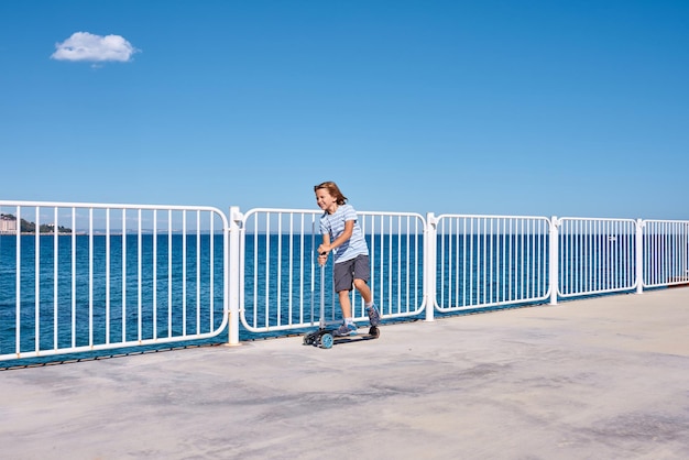 Junge, der an einem sonnigen Tag einen Roller auf einem Pier fährt