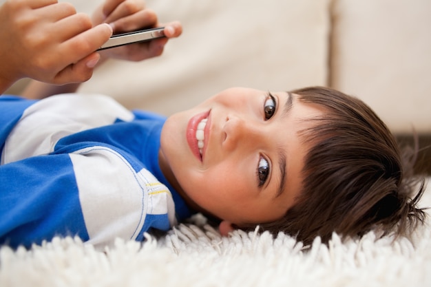 Junge, der auf dem Teppich mit Mobiltelefon liegt