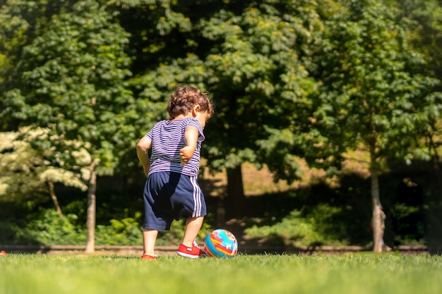 Junge, der Ball in einem Park spielt Erster Schritt und bereits den Ball tretend, der Spaß hat