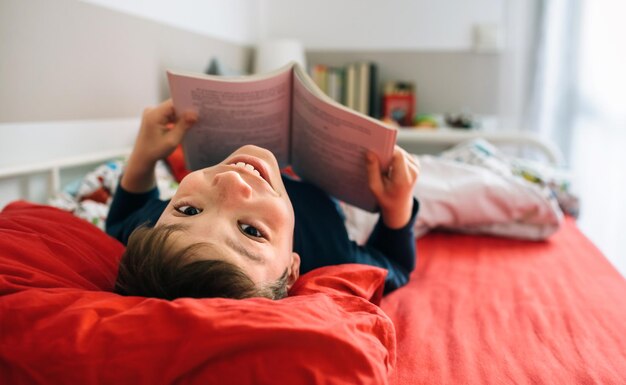 Junge, der beim Lesen eines Buches in die Kamera schaut