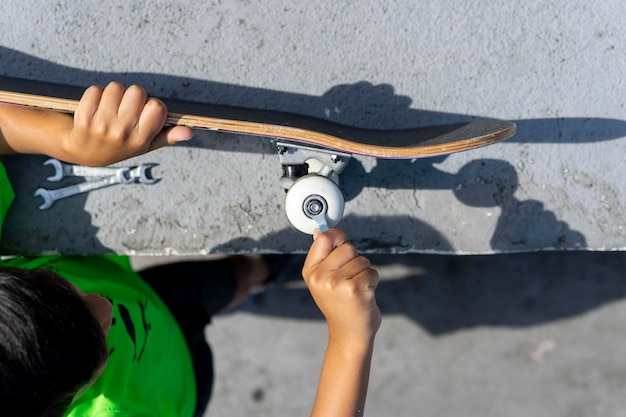 Junge, der das Rad seines Skateboards repariert, nachdem er es im Park der Skateboarder benutzt hat