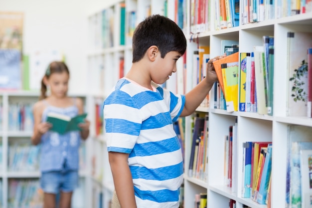 Junge, der ein Buch vom Bücherregal in der Bibliothek nimmt