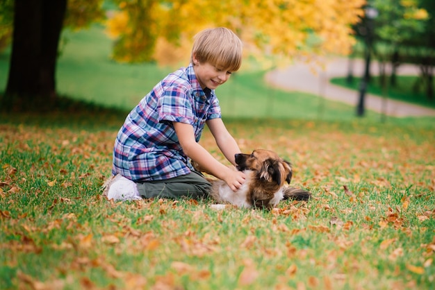 Junge, der einen Hund umarmt und im Herbst mit Stadtpark spielt