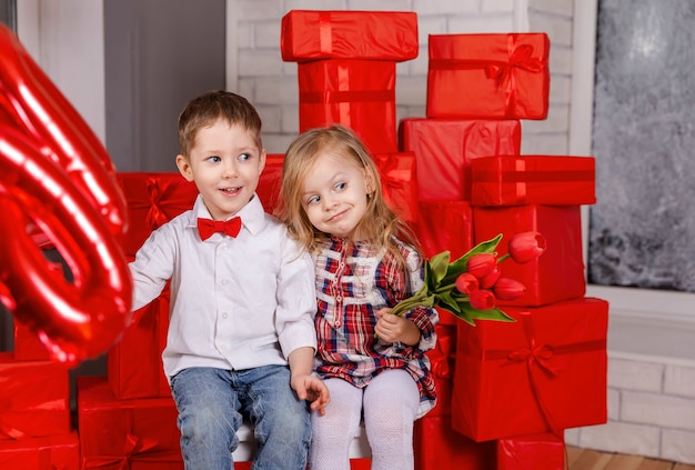 Junge, der Geschenk zum kleinen Mädchen im Valentinstag des lässigen Kleides präsentiert