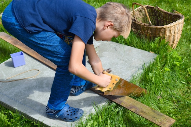 Junge, der Holz sägt. Ein Junge arbeitet im Garten. Kinderwerkstatt draußen