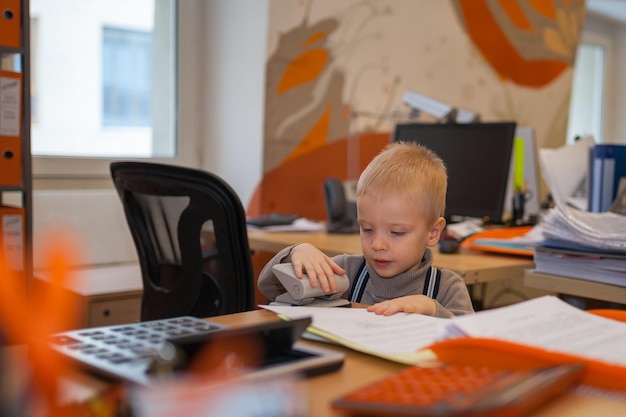 Junge, der im Büro mit Dokumenten spielt