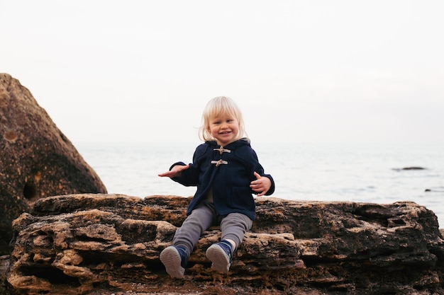 Junge, der im Herbst oder Sommer auf der Klippe am Meer sitzt