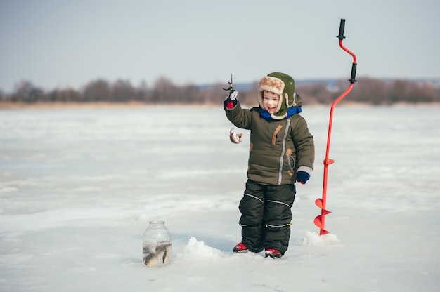 Junge, der im Winter fischt. Netter Junge fängt Fisch im Wintersee. Winter. Draussen