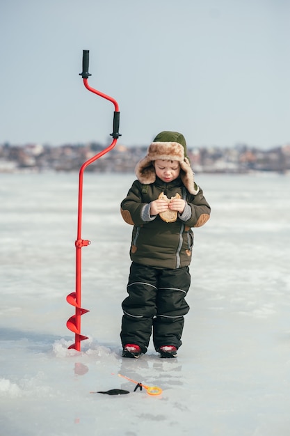 Junge, der im Winter fischt. Netter Junge fängt Fisch im Wintersee. Winter. Draussen