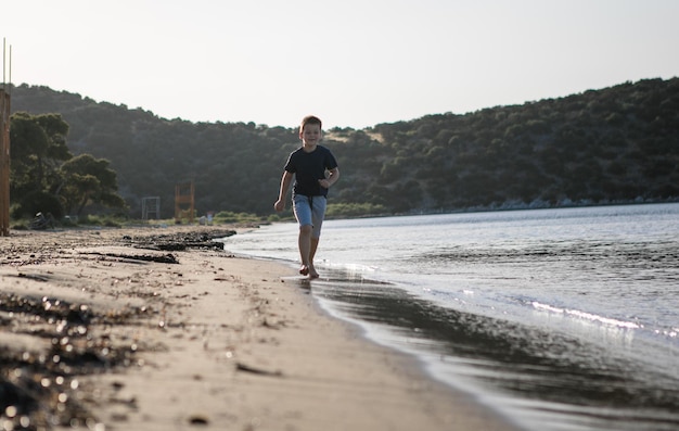 Junge, der in den Sommerferien am Strand spielt Kinder in der Natur mit schönem Meersand und blauem Laufen im Meerwasser