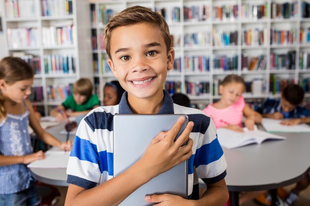 Junge, der Kamera mit Tabletten-PC in der Bibliothek betrachtet