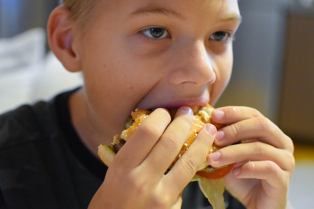 Junge, der köstlichen Fast-Food-Hamburger mit Pommes isst.