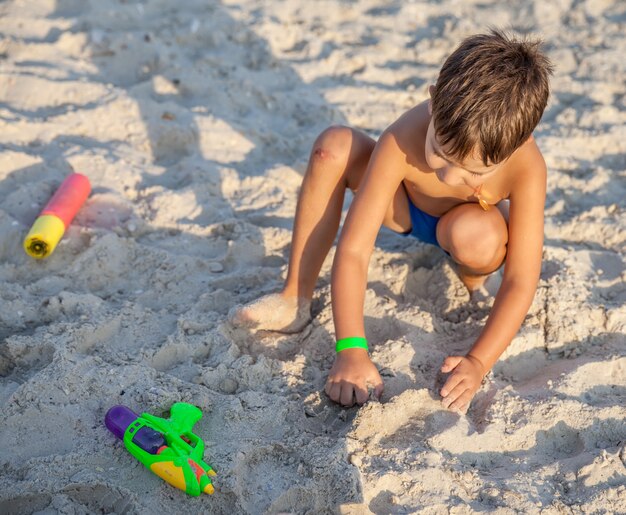 Junge, der mit Sand im Strand spielt