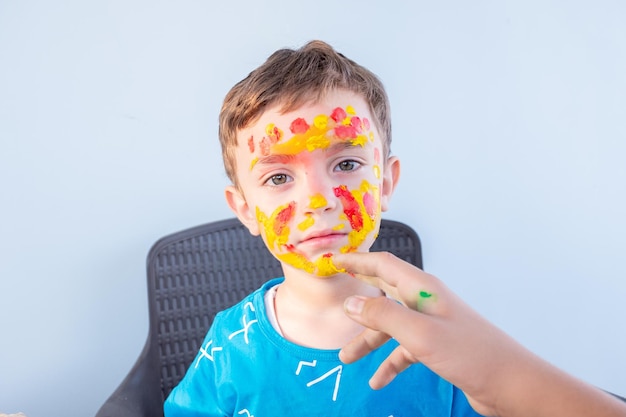 Junge, der mit seinen Händen und seinem Gesicht mit Farben spielt