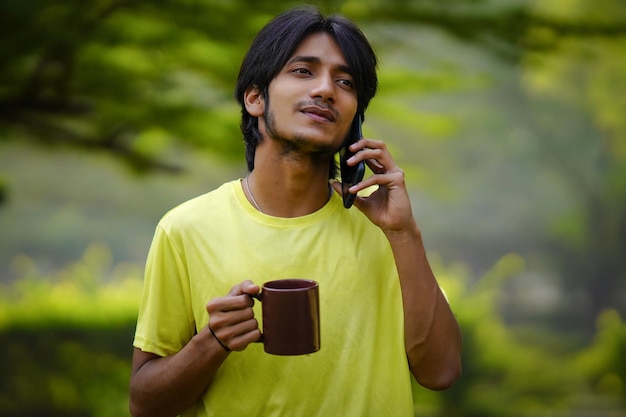 Junge, der morgens mit einer Kaffeetasse auf dem Bauernhof vom Handy spricht