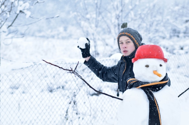 Junge, der Schneeballschlacht neben einem Schneemann spielt, lustige Winteraktivitäten