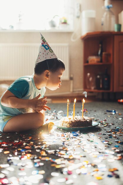 Junge, der seinen Geburtstag feiert, bläst Kerzen auf hausgemachtem gebackenem Kuchen, der auf dem Geburtstagspa...