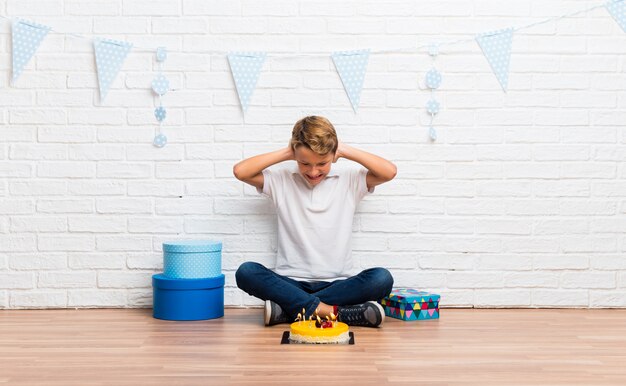 Junge, der seinen Geburtstag mit einem Kuchen feiert, der beide Ohren mit den Händen bedeckt