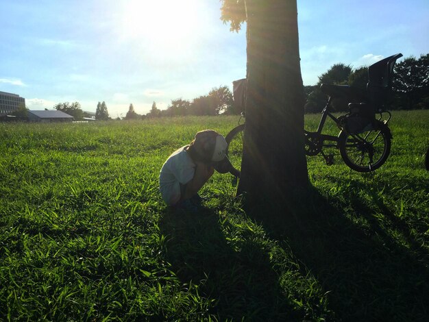 Foto junge, der sich am baum auf dem grasbewachsenen feld im park hockt