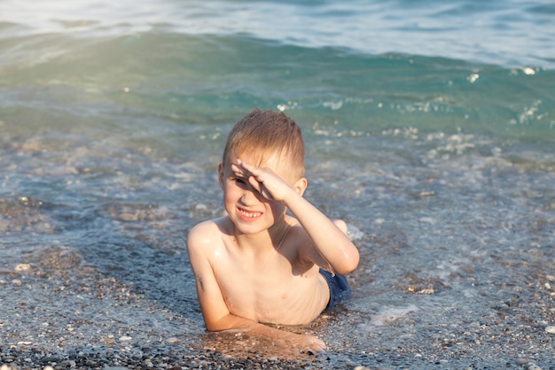 Junge, der sich an einem sonnigen Sommertag im Meer oder in den Meereswellen amüsiert. Ozeanküste und Strand. Aktiver Lebensstil und Erholungskonzept.