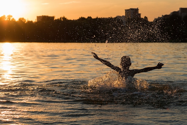 Junge, der Wasser im Fluss bei Sonnenuntergang spritzt. Silhouette Rahmen