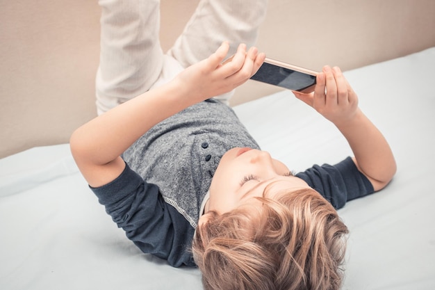 Junge, der zu Hause mit den Füßen hoch auf dem Bett auf dem Handy spielt