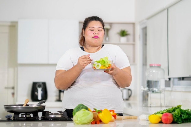 Junge dicke Frau isst leckeren Salat in der Küche